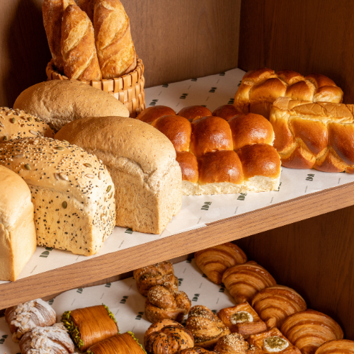 Fresh baked breads and viennoiserie pastries displayed on wooden shelves at IDA Bakery, including sourdough loaves, brioche buns, baguettes, and croissants